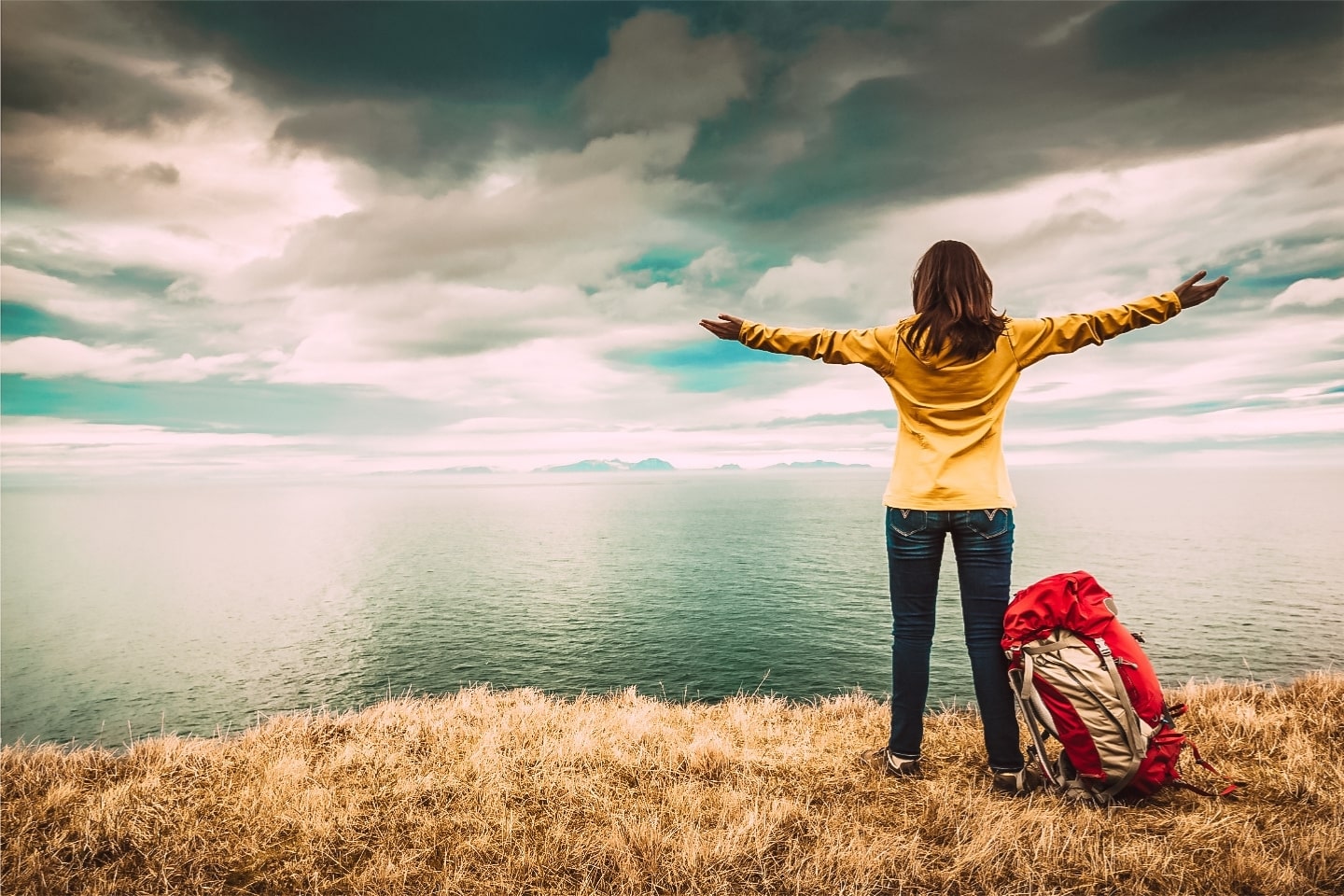 backpacker looking our over the ocean with her arms rasied