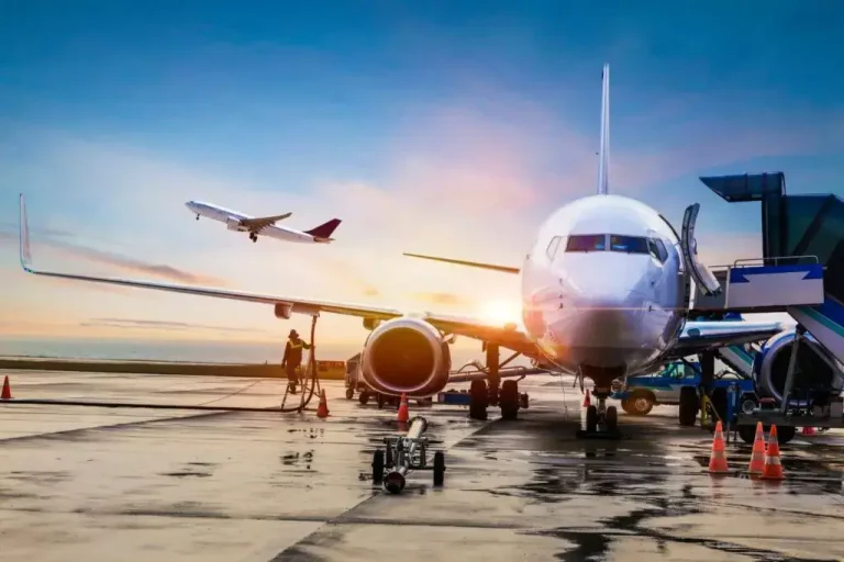 on the tarmac. airplane is front on with another airplane taking off to the left in the background. there is a gorgeous sun set